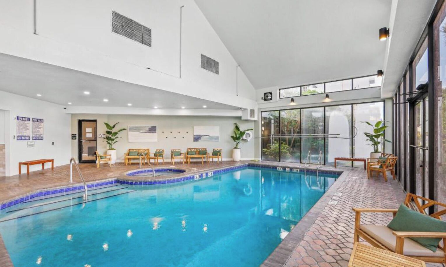 An indoor swimming pool with a sun terrace, lounge chairs, and a view of the outside.