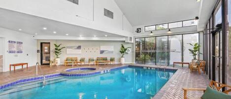 An indoor swimming pool with a sun terrace, lounge chairs, and a view of the outside.