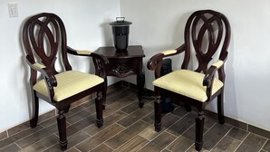 Two wooden chairs with cushioned seats, a small table with a black container, and a framed picture on the wall.