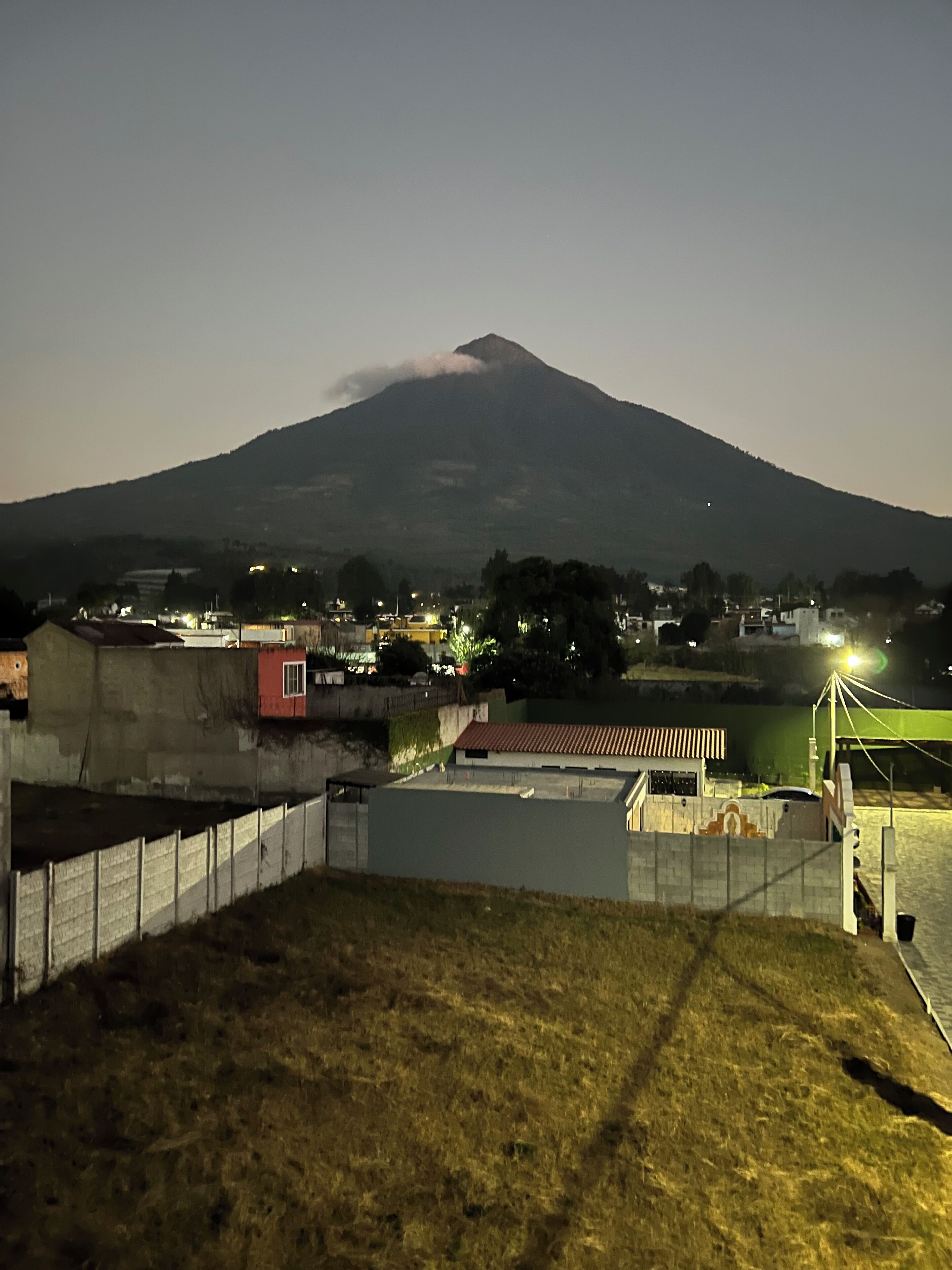 A nighttime view of a mountain with a small town in the foreground, featuring a fenced area and a water body.
