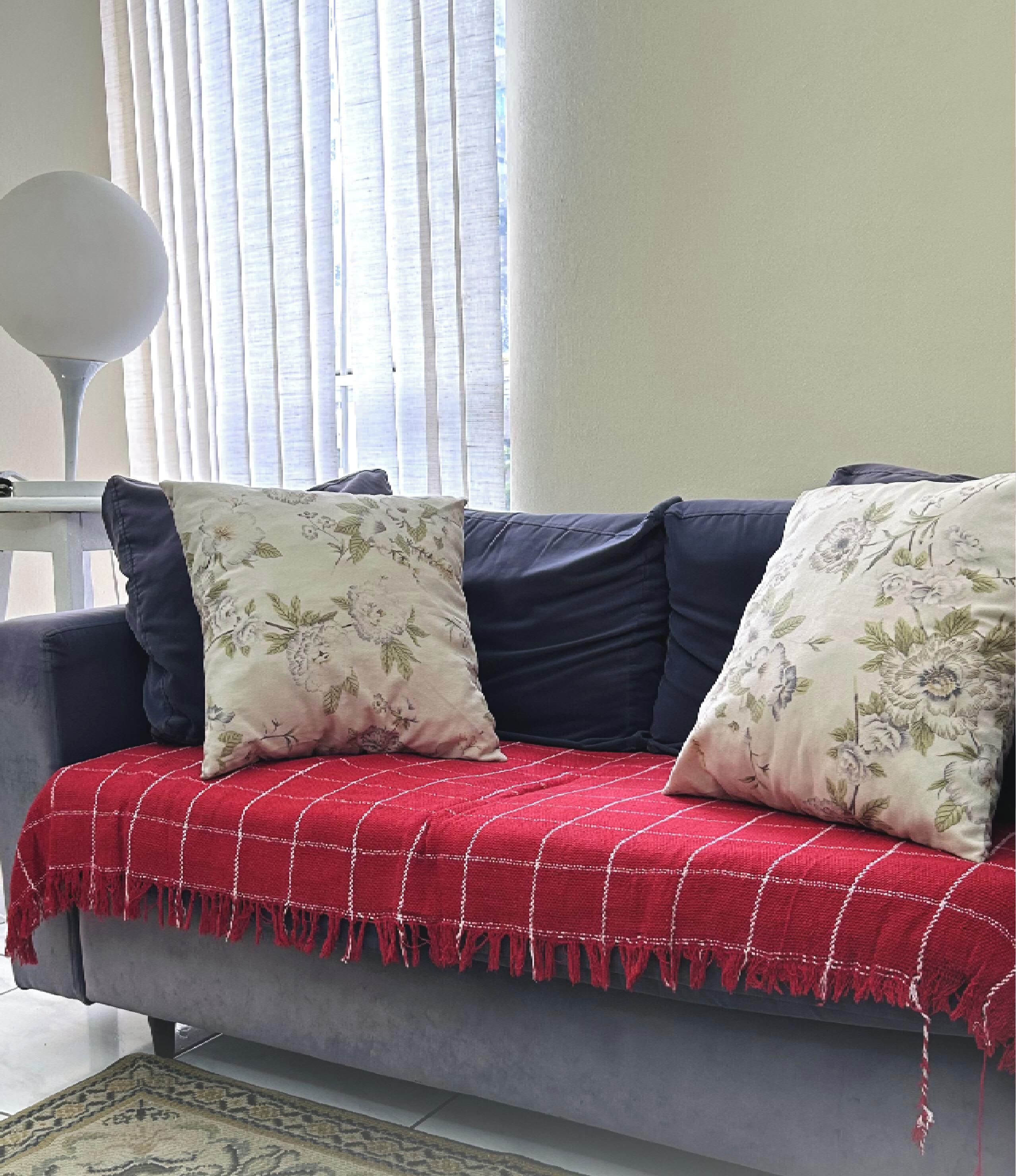 A grey sofa with a red and white checkered throw blanket, two floral pillows, and a dark blue cushion.