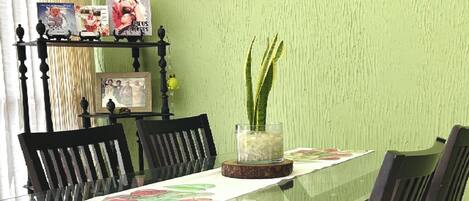 A dining area with a glass table, chairs, and a fruit painting on the wall.