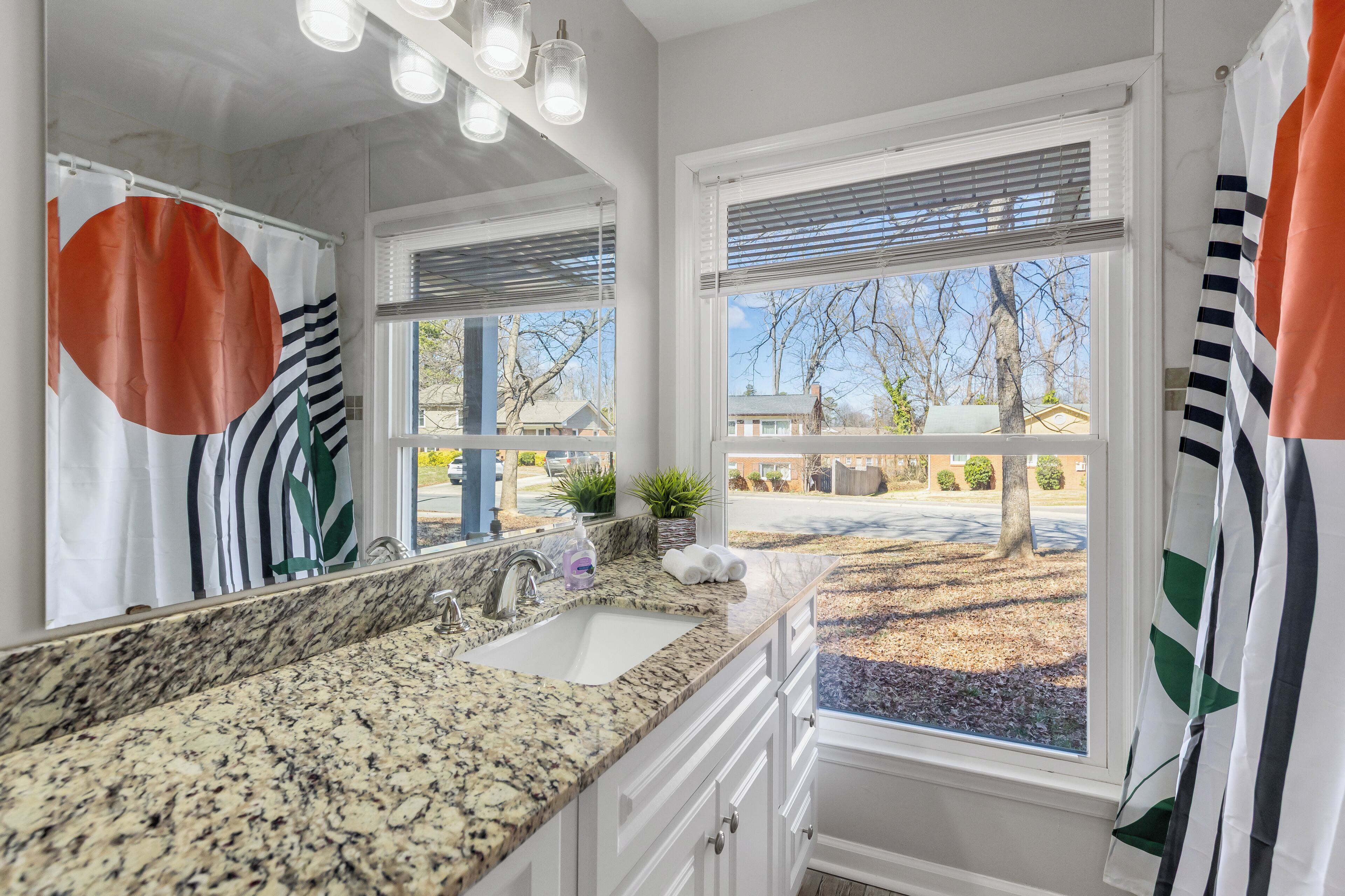 A bathroom with a granite countertop, a sink, a mirror, and a window with blinds.
