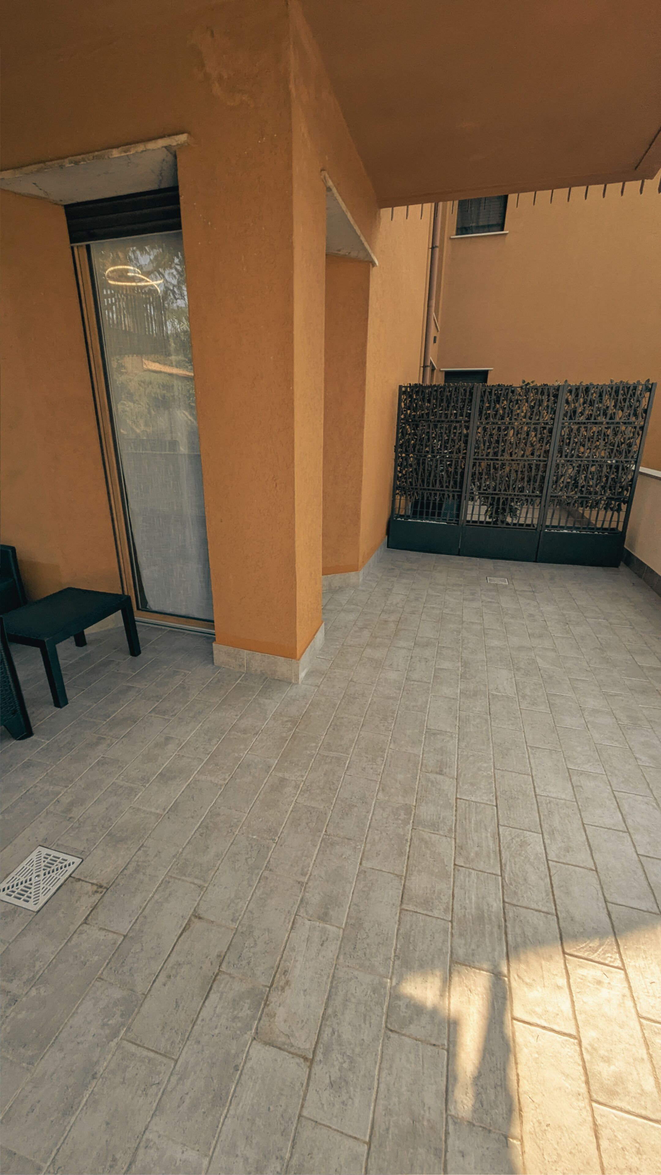 A covered outdoor area with tiled flooring, a bench, a door, and a metal gate.