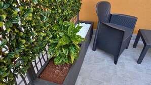 A patio area with a black wicker chair, a small table, a white pebbled planter, and a green hedge against a yellow wall. - Sfreg Suites Magenta - camere e B&B (Magenta)