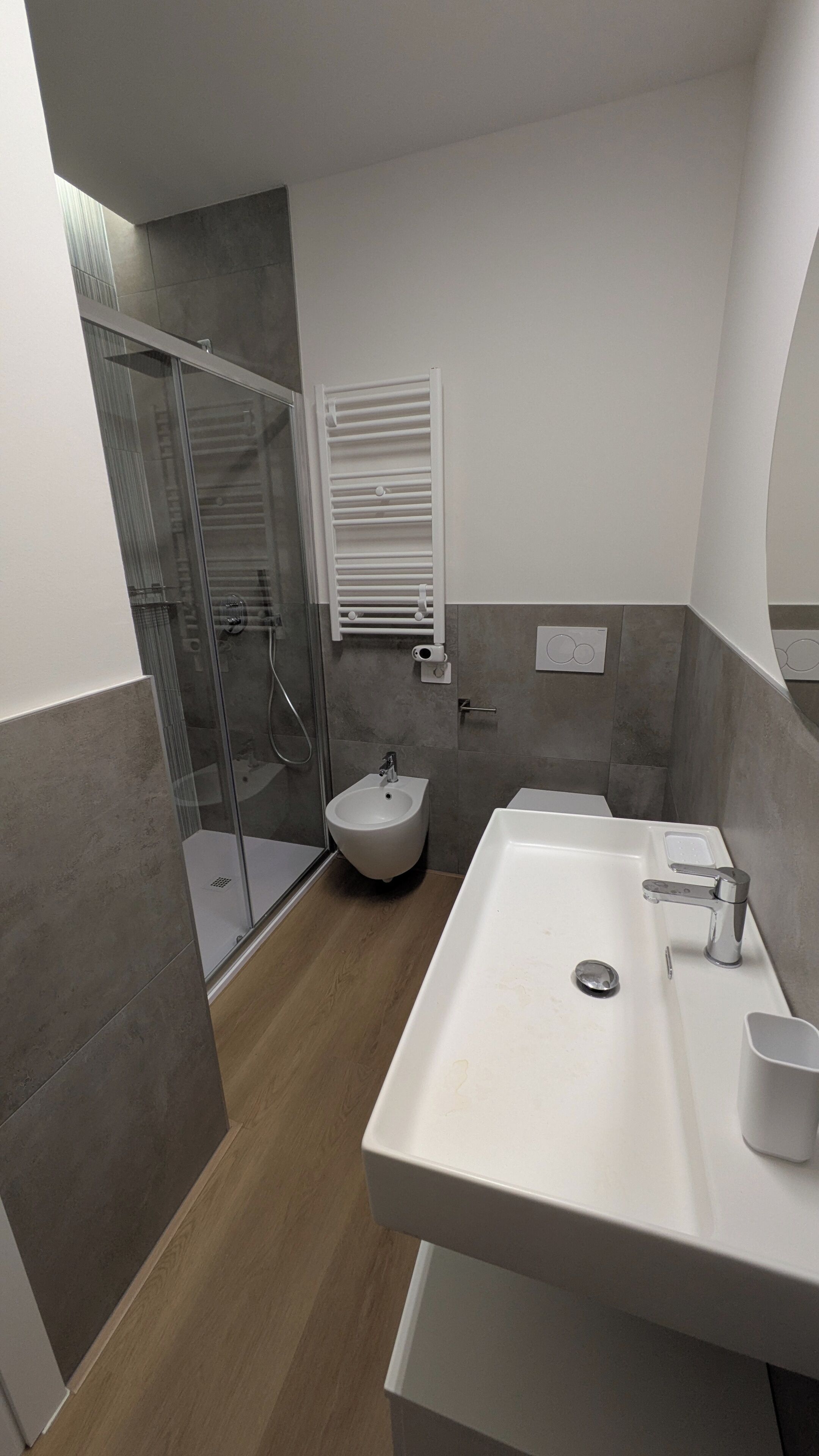 Une salle de bain moderne avec une douche à parois de verre, un bidet, un lavabo avec un miroir et un porte-serviettes.