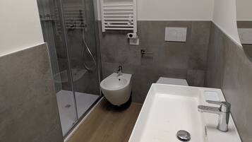 Une salle de bain moderne avec une douche à parois de verre, un bidet, un lavabo avec un miroir et un porte-serviettes.