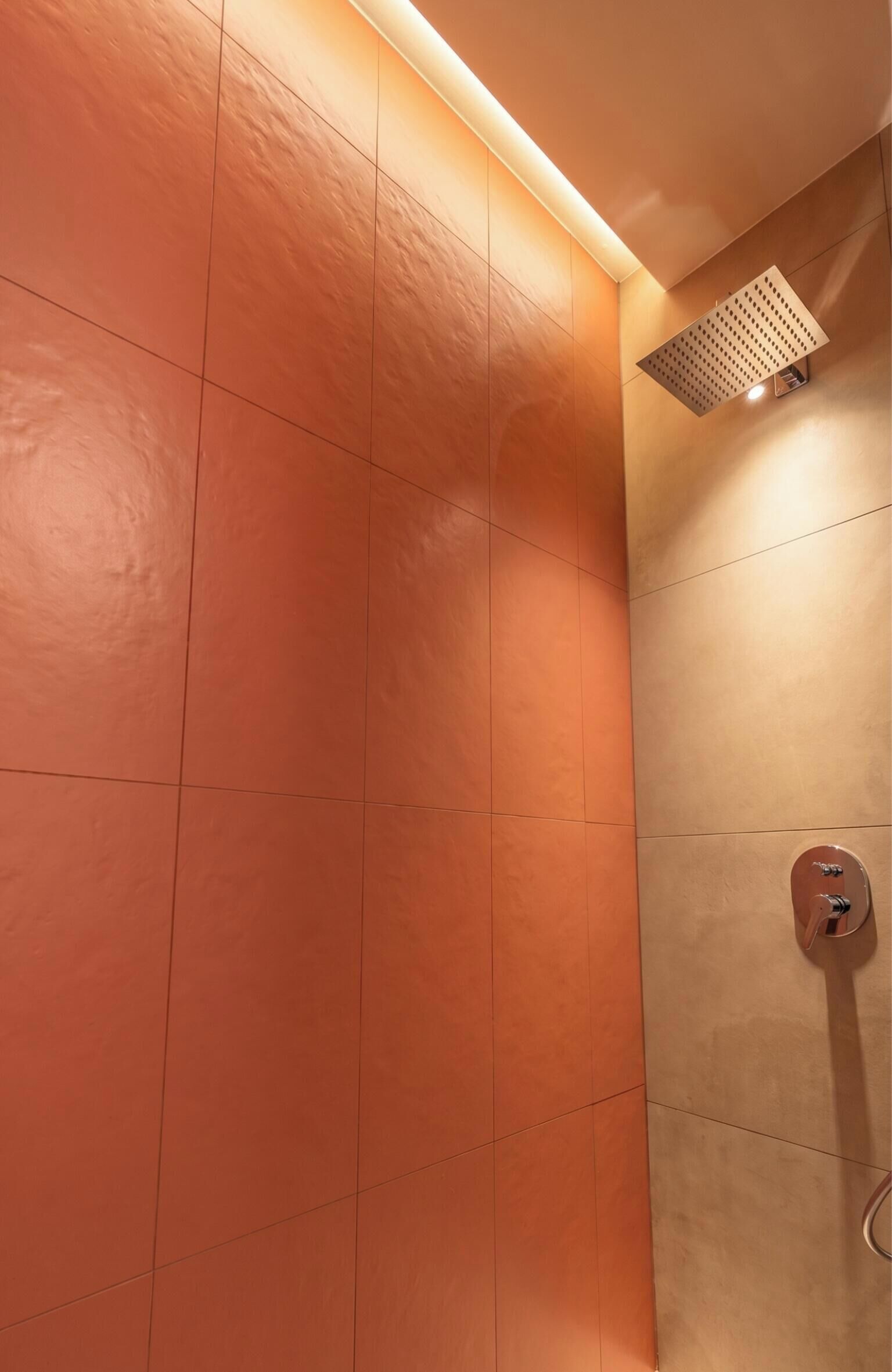 Ein Badezimmer mit orangefarben gefliesten Wänden, einer Duschbrause und einer wandmontierten Leuchte.