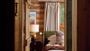 Un intérieur en bois comprenant un lit, une table de chevet, une lampe, un tableau encadré et une fenêtre avec des rideaux.