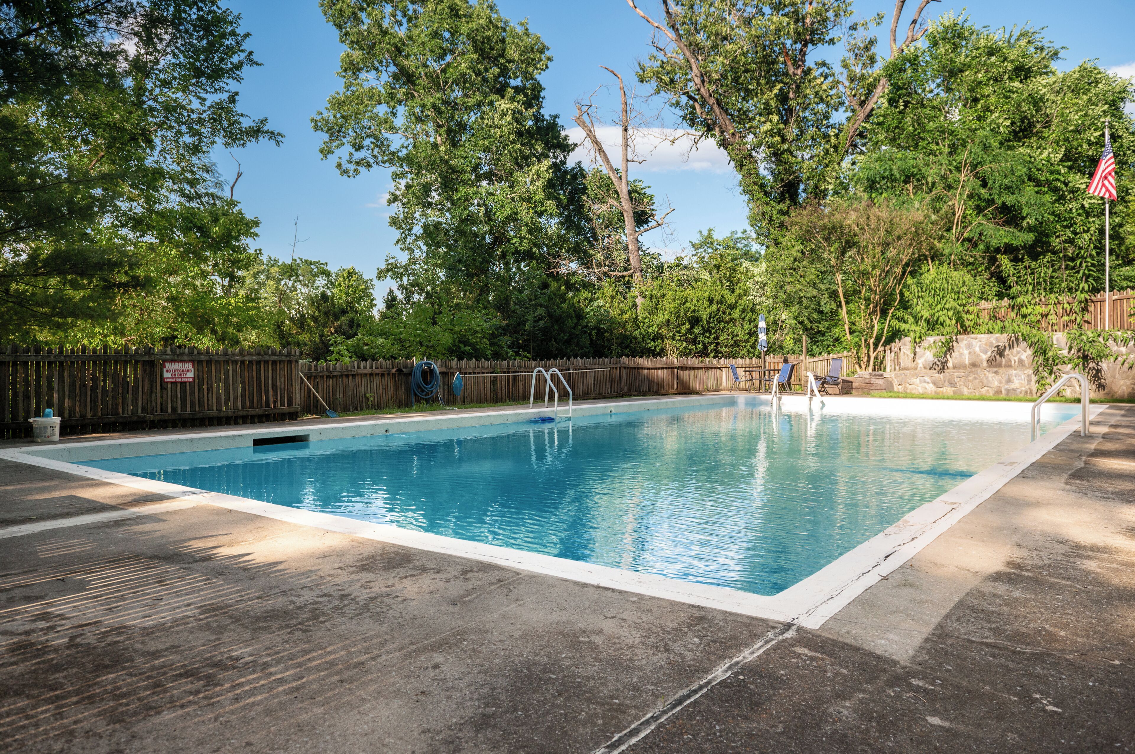 Una piscina rectangular con muelle de madera, rodeada de árboles y valla de madera.