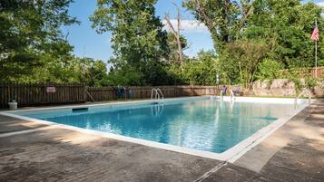 Una piscina rectangular con muelle de madera, rodeada de árboles y valla de madera.