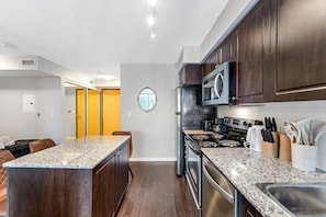 A modern kitchen with granite countertops, dark wood cabinets, stainless steel appliances, and a central island. - Queen Verity Suites (Toronto)