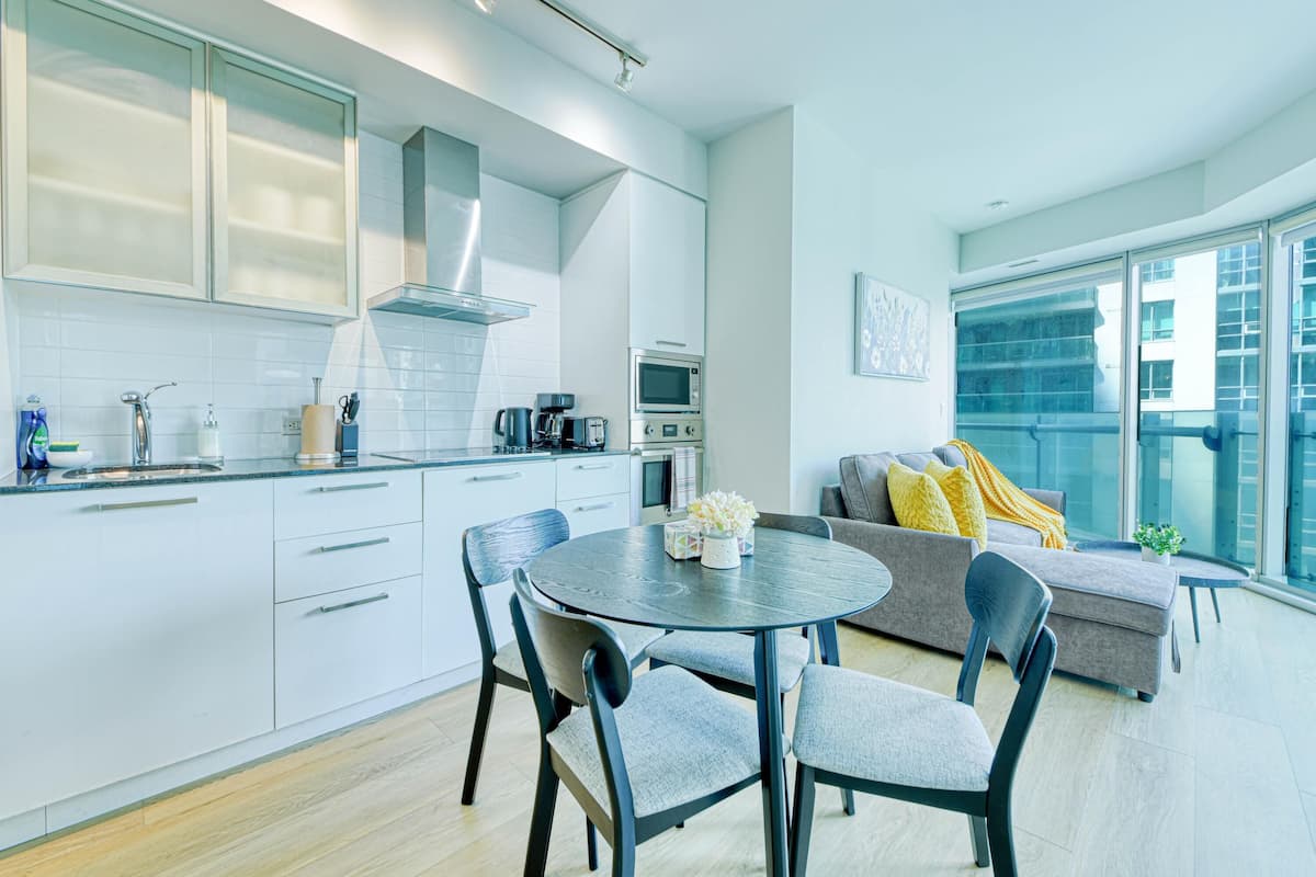 A modern kitchen with white cabinets, a round dining table, and a gray sofa with yellow cushions.