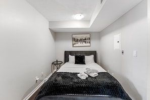 A hotel room with a bed, a nightstand, a wall-mounted light, and a framed picture. - Queen Verity Suites (Toronto)