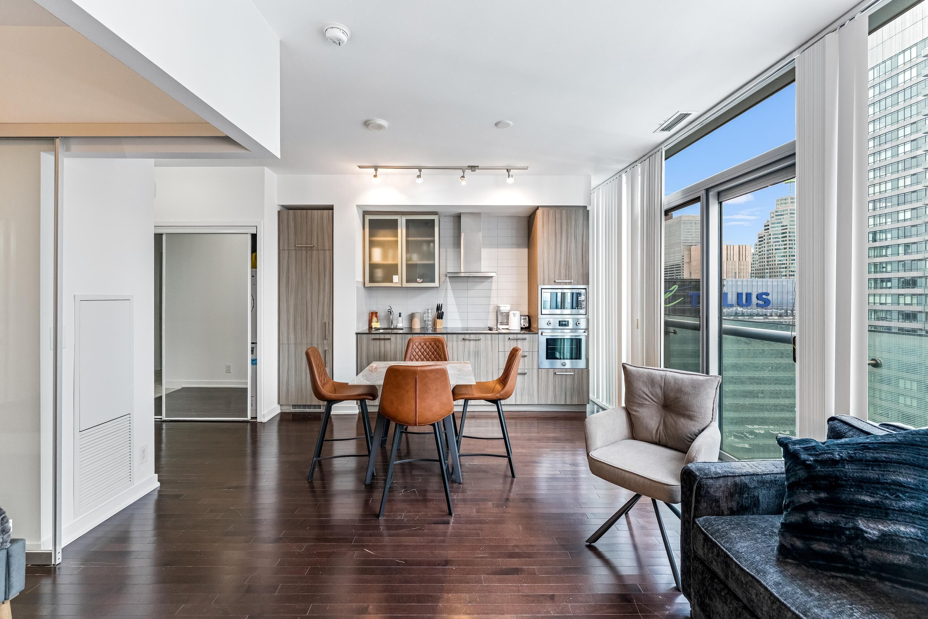 A modern apartment with a dining area, kitchen, and large windows offering a city view.