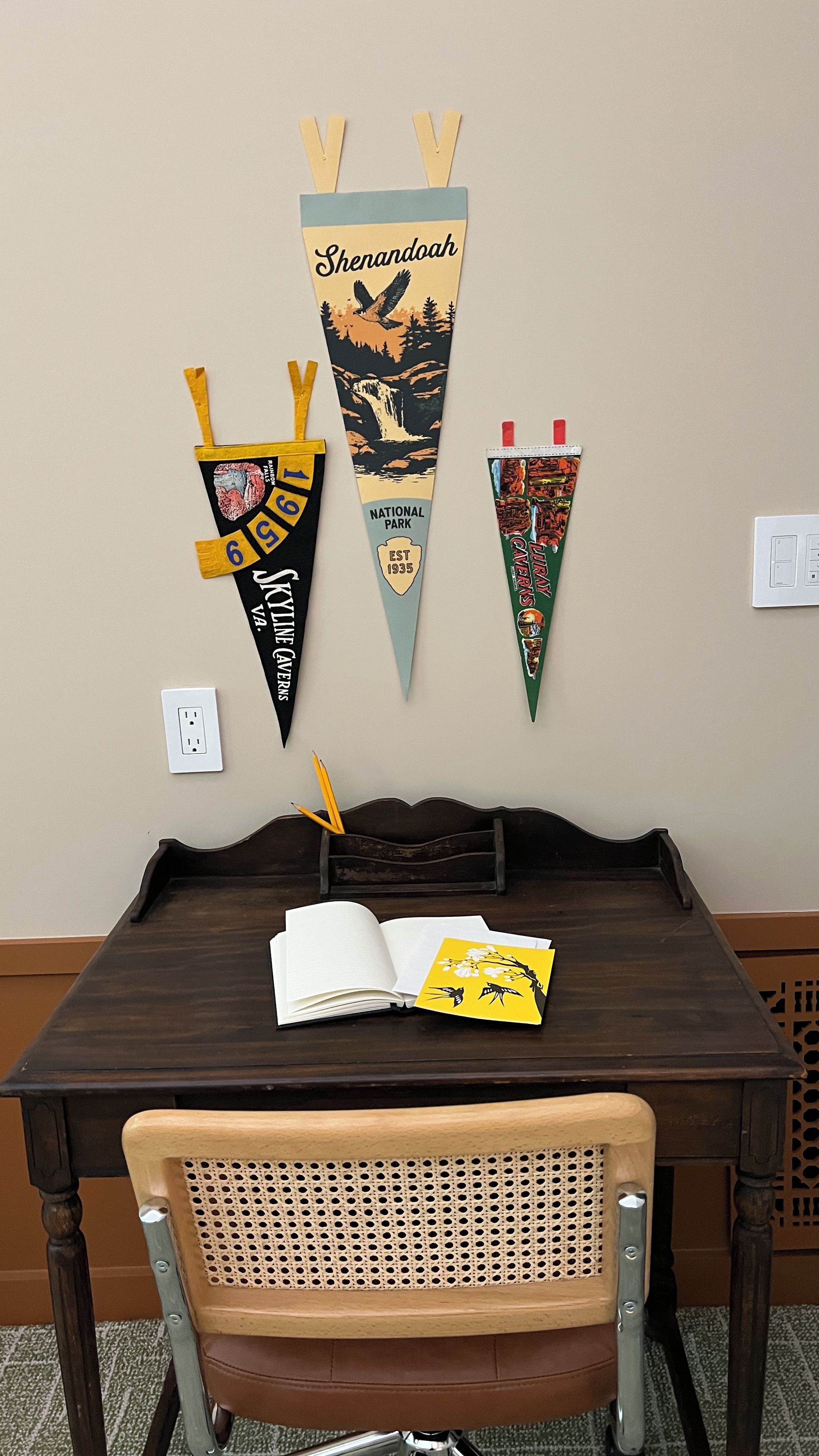 A wooden table with a book and a yellow card, a chair, and three triangular banners on the wall.
