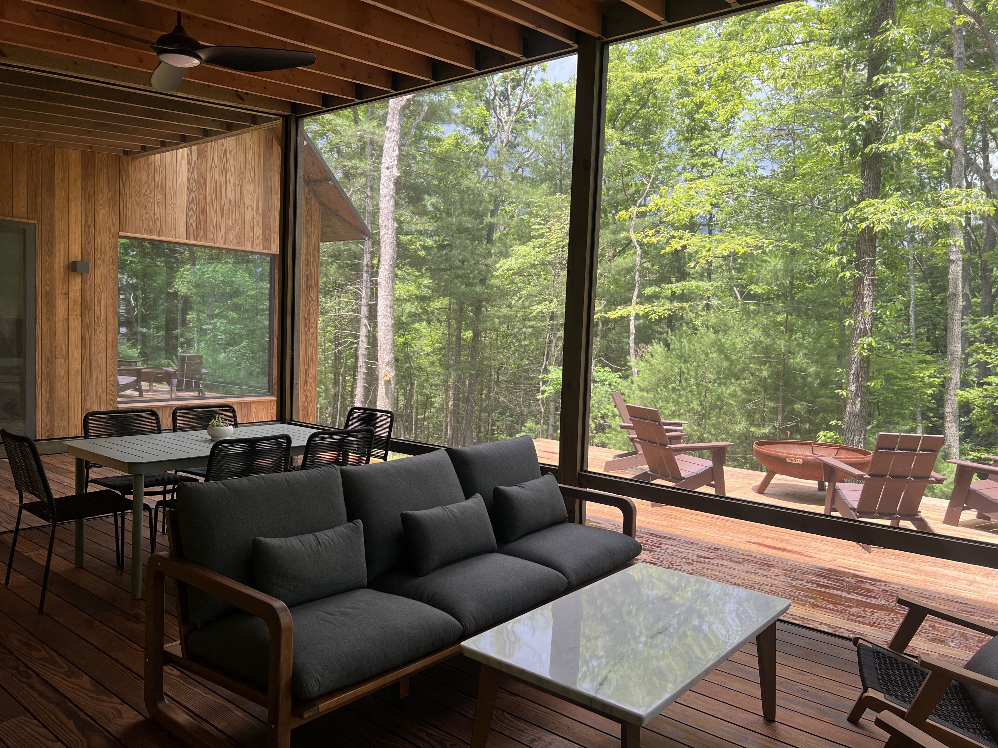Una moderna baita con un'ampia terrazza, un'area pranzo e un divano con vista su una foresta.