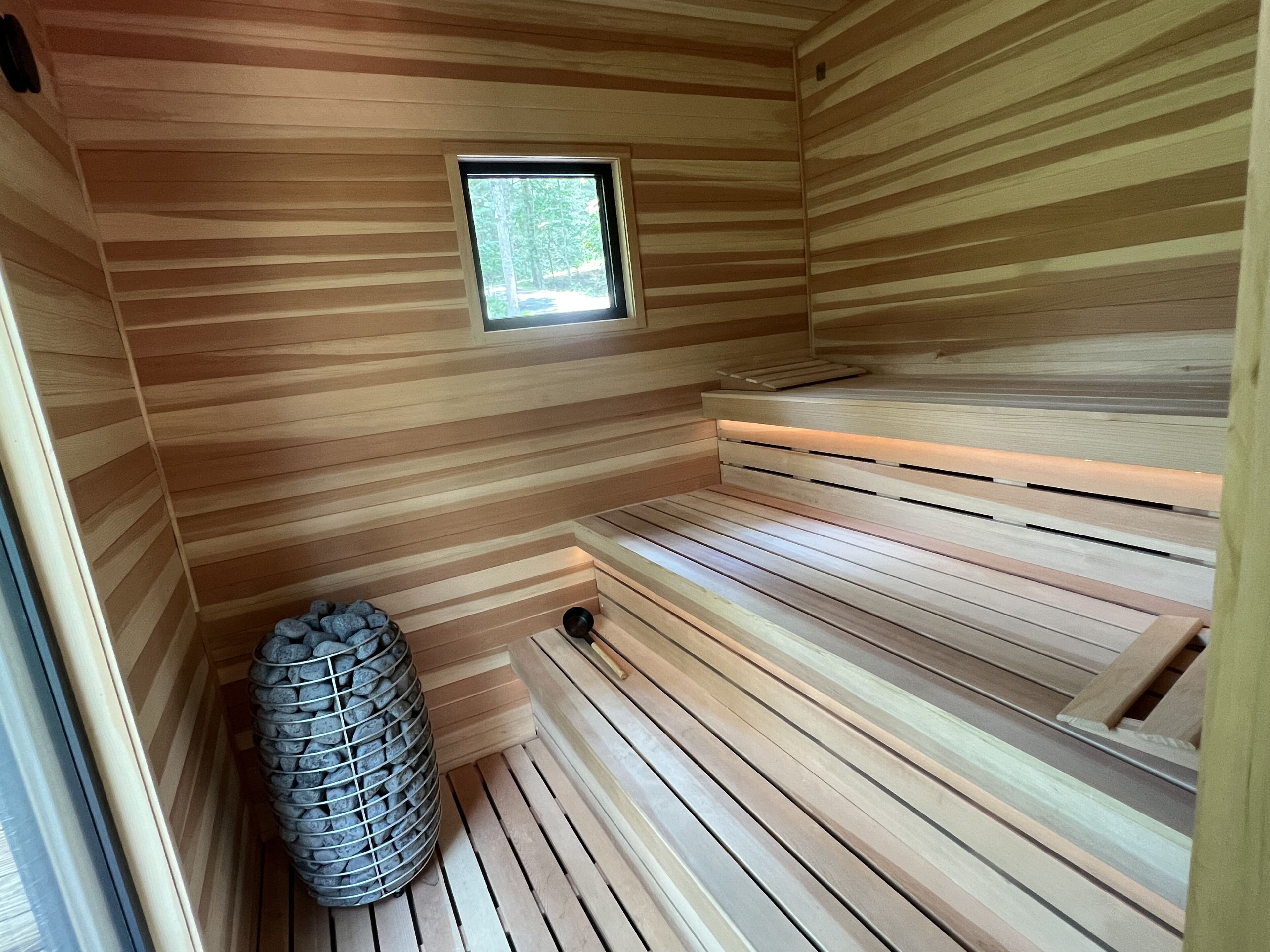 Eine Sauna mit Holzlamellen, einem kleinen Fenster und einem Steinofen.
