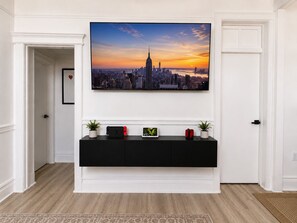 A hallway with a large cityscape painting, a black console table with small plants, and a patterned rug. - NYC Skyline Views 20 min to Times Square Sleeps 11 (West New York)