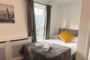 Een hotelkamer met een bed, een raam met gordijnen, een radiator en een aan de muur hangend schilderij.