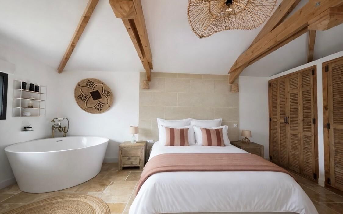A bedroom with a large bathtub, wooden beams, a round wall decoration, and a wardrobe.