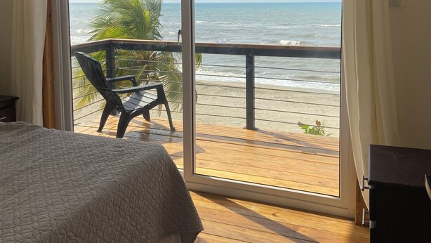 A bedroom with a large sliding glass door leading to a balcony with a view of the beach.