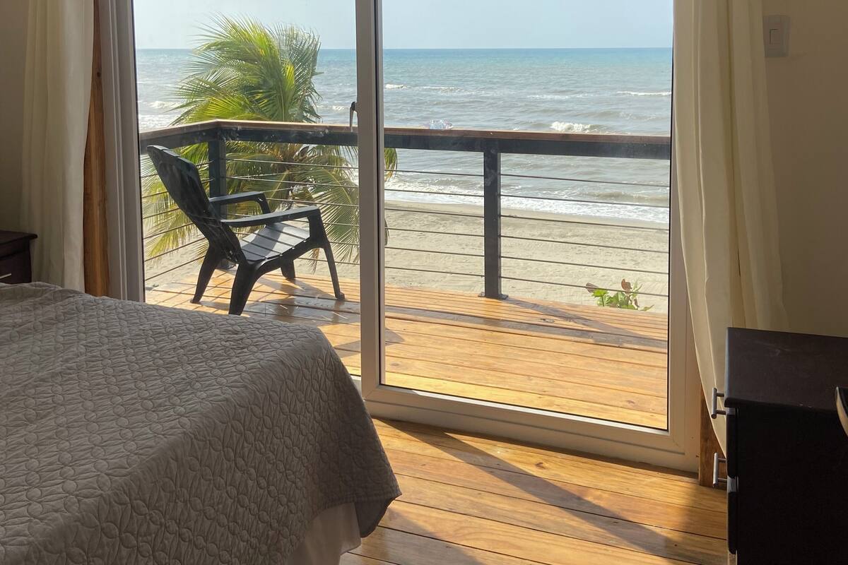 A bedroom with a large sliding glass door leading to a balcony with a view of the beach.
