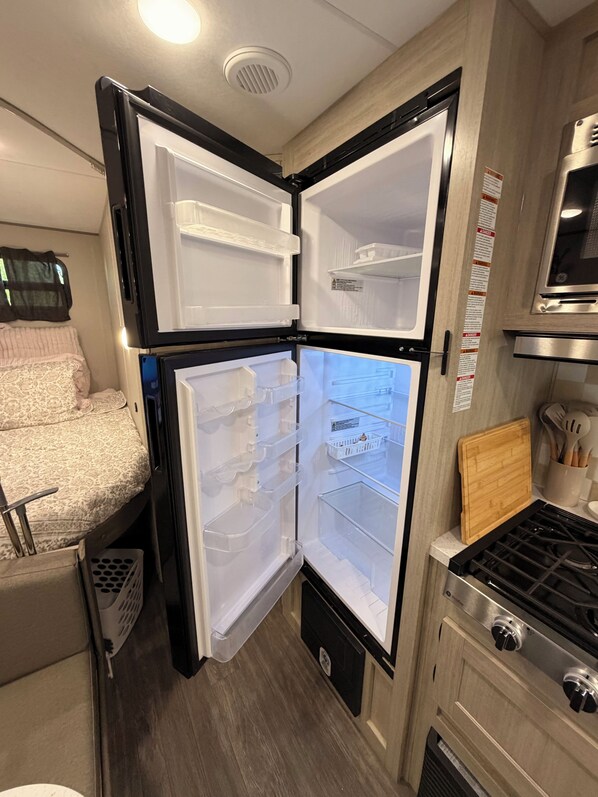A compact kitchen with a built-in refrigerator, a stove, and a small countertop. - Sundown Serenity, New 2026 RV with Porch (Springtown)