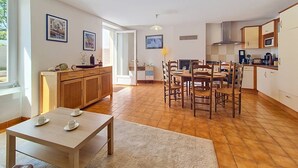 Een ruime keuken met houten kastjes, een eethoek met een tafel en stoelen, en een groot raam dat voor natuurlijk licht zorgt.