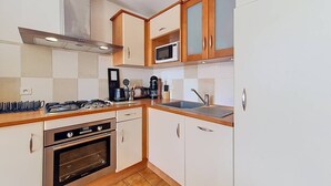 Een kleine keuken met een gasfornuis, oven, magnetron en spoelbak.