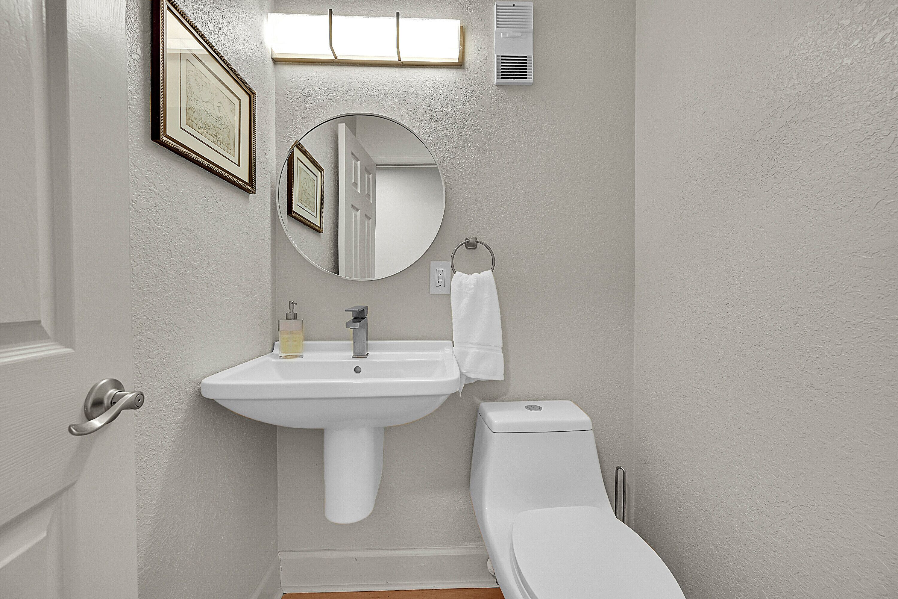 A bathroom with a sink, toilet, mirror, and framed pictures on the wall.