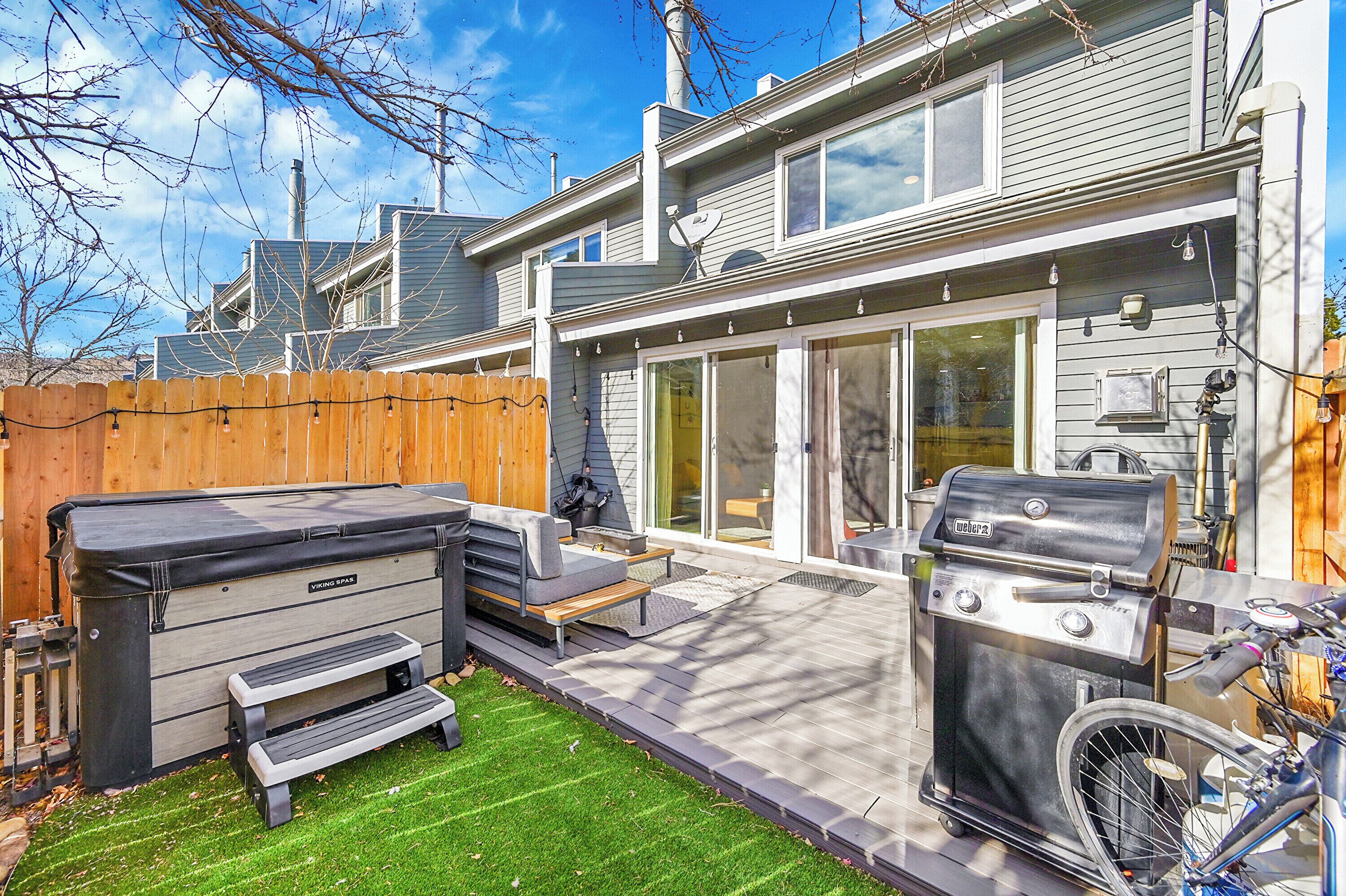 Ein Garten mit Whirlpool, Grill und Holzzaun.