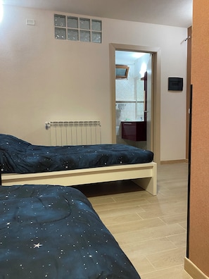 Ein Schlafzimmer mit zwei Betten, einem Heizkörper, einem Fenster mit Jalousien und einer Tür zu einem Badezimmer.