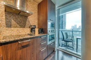 A modern kitchen with wooden cabinets, a stainless steel range hood, and a view of a cityscape through a large window. - Queen West House (Toronto)