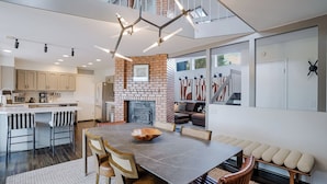 Eine moderne Küche mit Kamin aus Ziegeln, ein Essbereich mit großem Tisch und Stühlen sowie ein Schlafbereich mit Balkon.