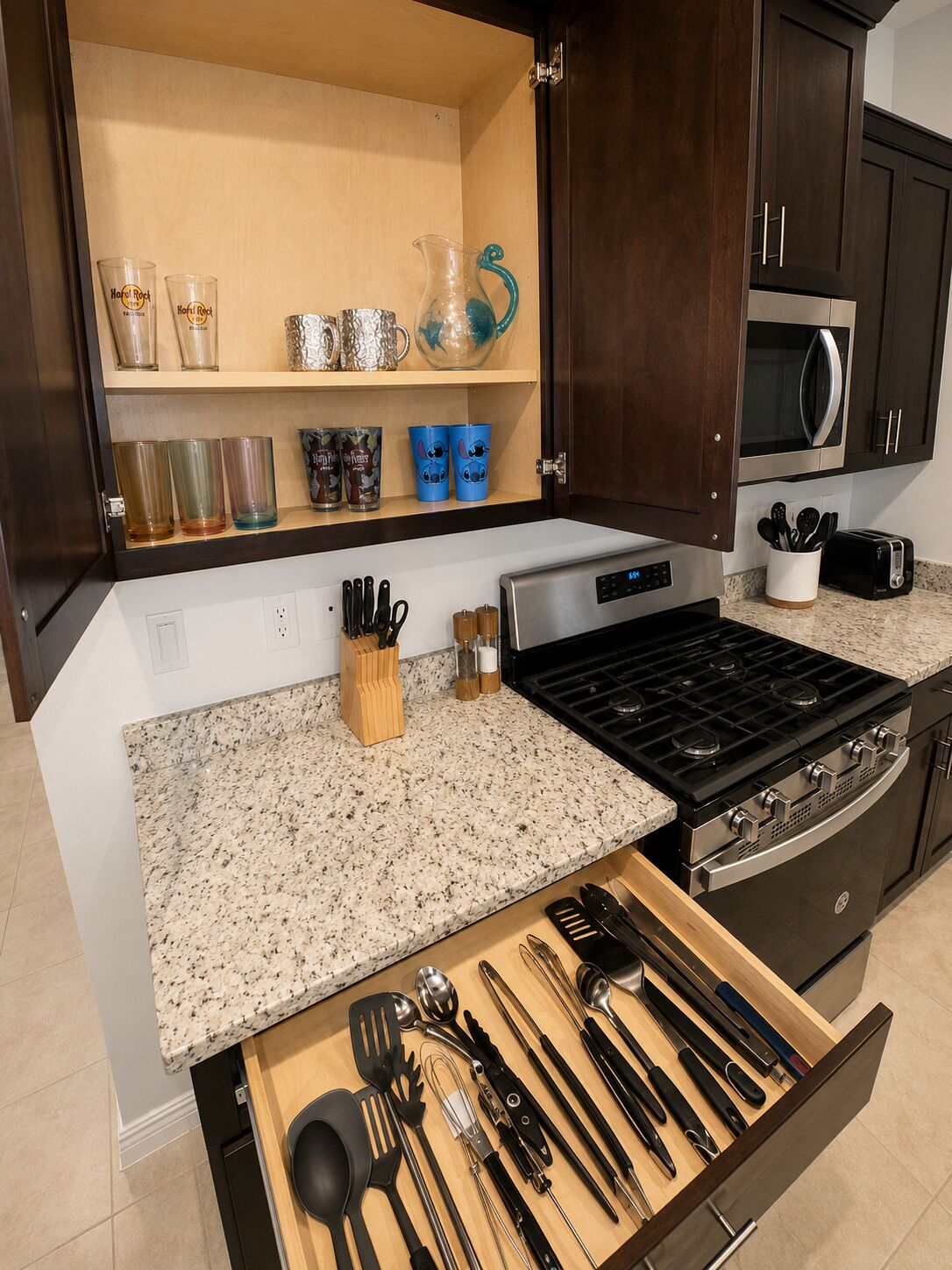 A kitchen with a granite countertop, stainless steel appliances, and a variety of utensils in a drawer.