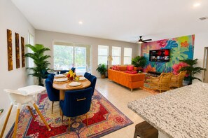 Ein modernes Wohnzimmer mit Essbereich, einer Couch, einem Fernseher und einem Deckenventilator.
