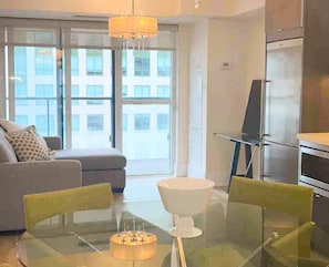 A modern living room with a glass dining table, a sofa, and a large window offering a city view. - West Queen Atelier (Toronto)