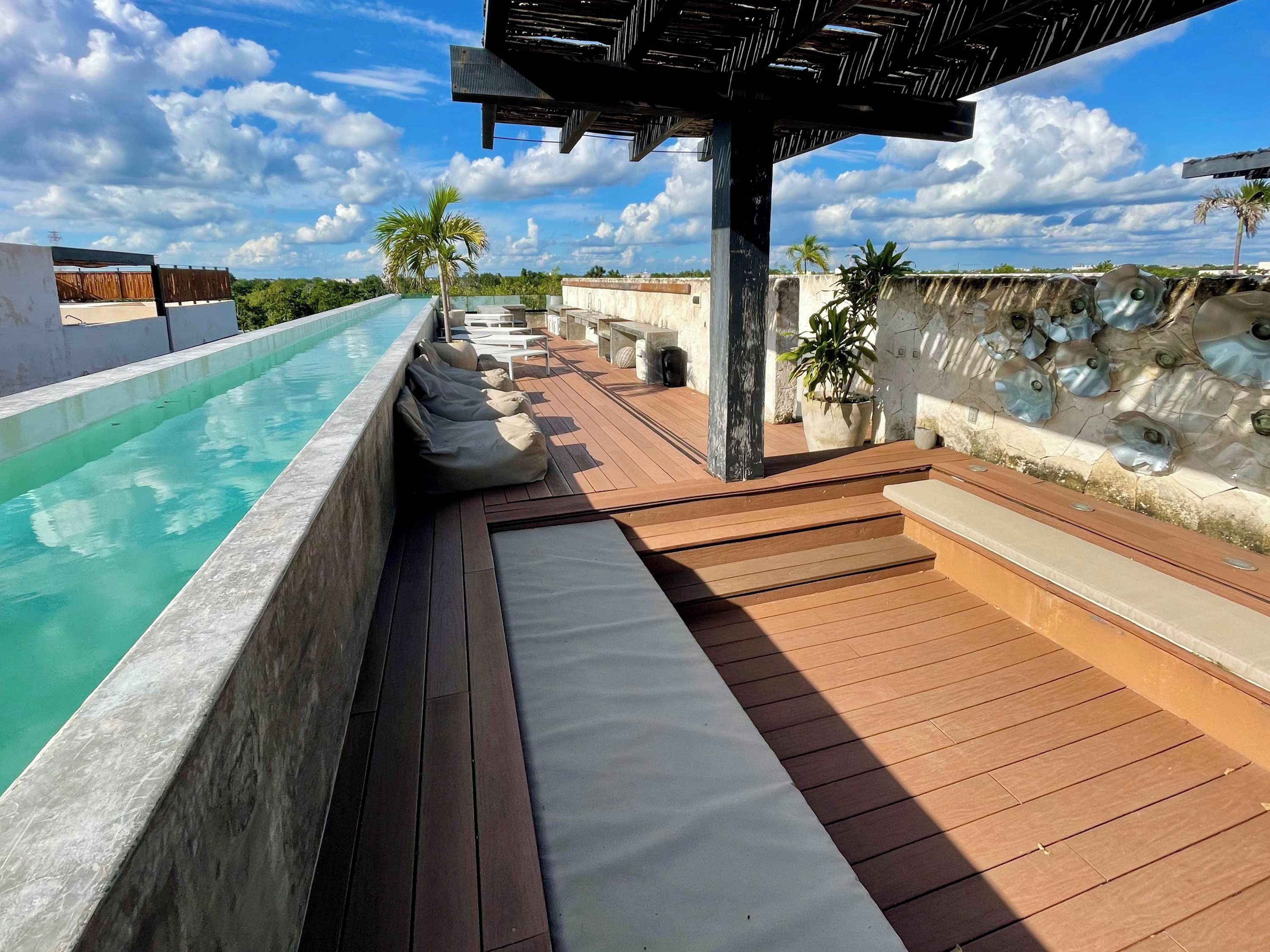Un espace piscine aménagé sur le toit, avec une terrasse en bois, des chaises longues et une pergola.