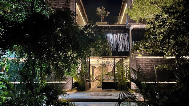 A modern building with a stone facade, a curved entrance, and a well-lit interior. - Black House - Stylish 3BR in Aldea Zama with Rooftop (Tulum)