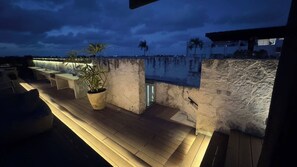 Un bar en la azotea con paredes de piedra, mesas al aire libre y una planta en maceta.