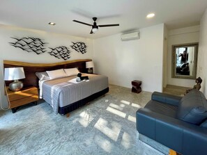A hotel room with a bed, bedside tables, a ceiling fan, wall art, an air conditioning unit, a mirror, and a sofa. - Black House - Stylish 3BR in Aldea Zama with Rooftop (Tulum)