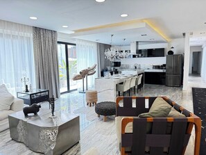 A modern living room with a sofa, a coffee table, and a dining area with chairs. - Black House - Stylish 3BR in Aldea Zama with Rooftop (Tulum)