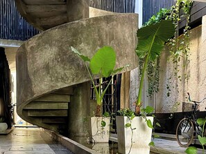 A spiral staircase with concrete walls, potted plants, and a bicycle. - Black House - Stylish 3BR in Aldea Zama with Rooftop (Tulum)