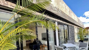 A modern building with large glass windows, a stone facade, and outdoor seating area with white chairs and a table. - Black House - Stylish 3BR in Aldea Zama with Rooftop (Tulum)