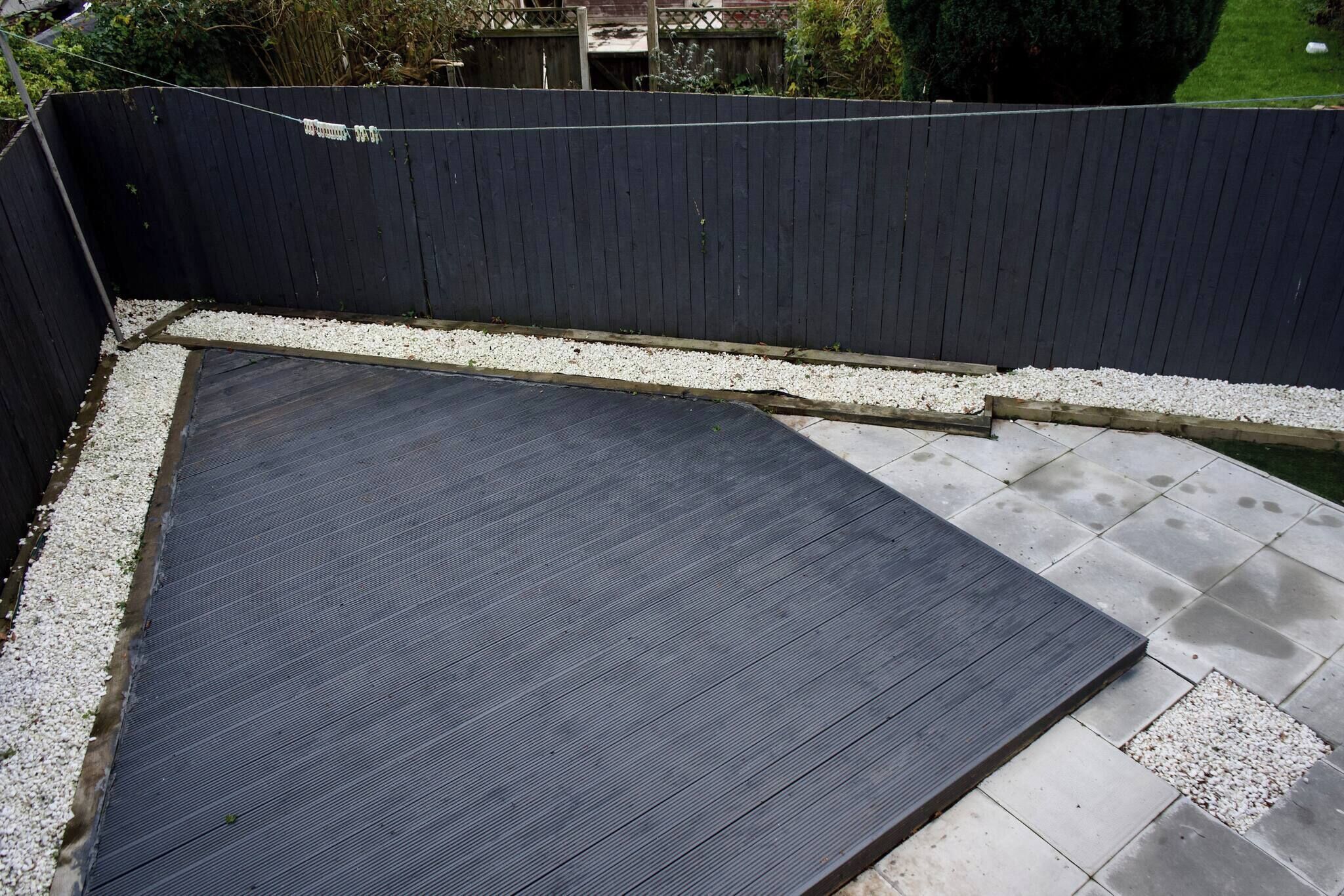 Terraço no telhado com piso de madeira escura, borda de brita branca e vista para uma área residencial.