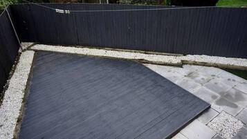 Terraço no telhado com piso de madeira escura, borda de brita branca e vista para uma área residencial.