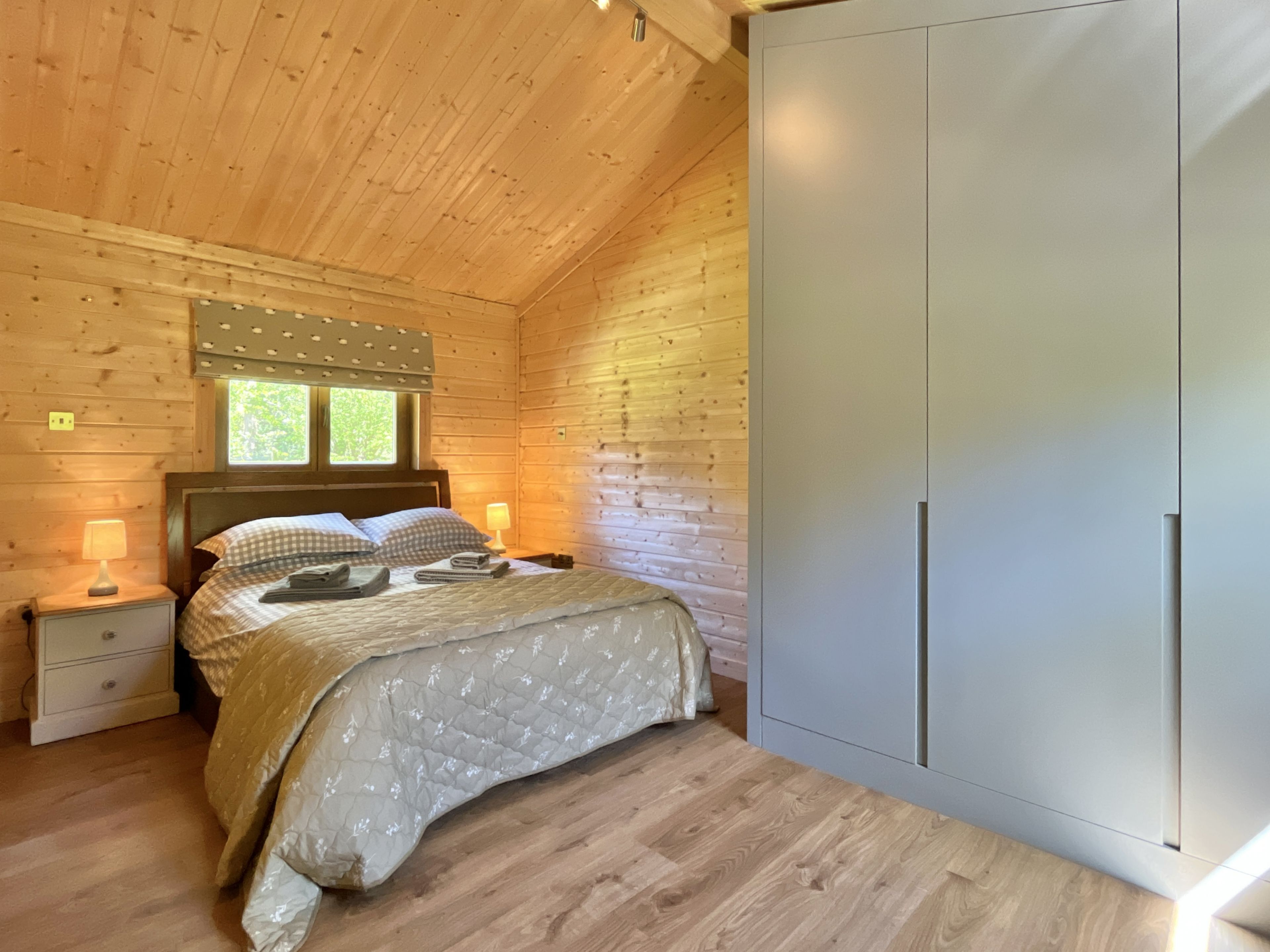 A wooden cabin bedroom with a bed, nightstands, and a wardrobe.
