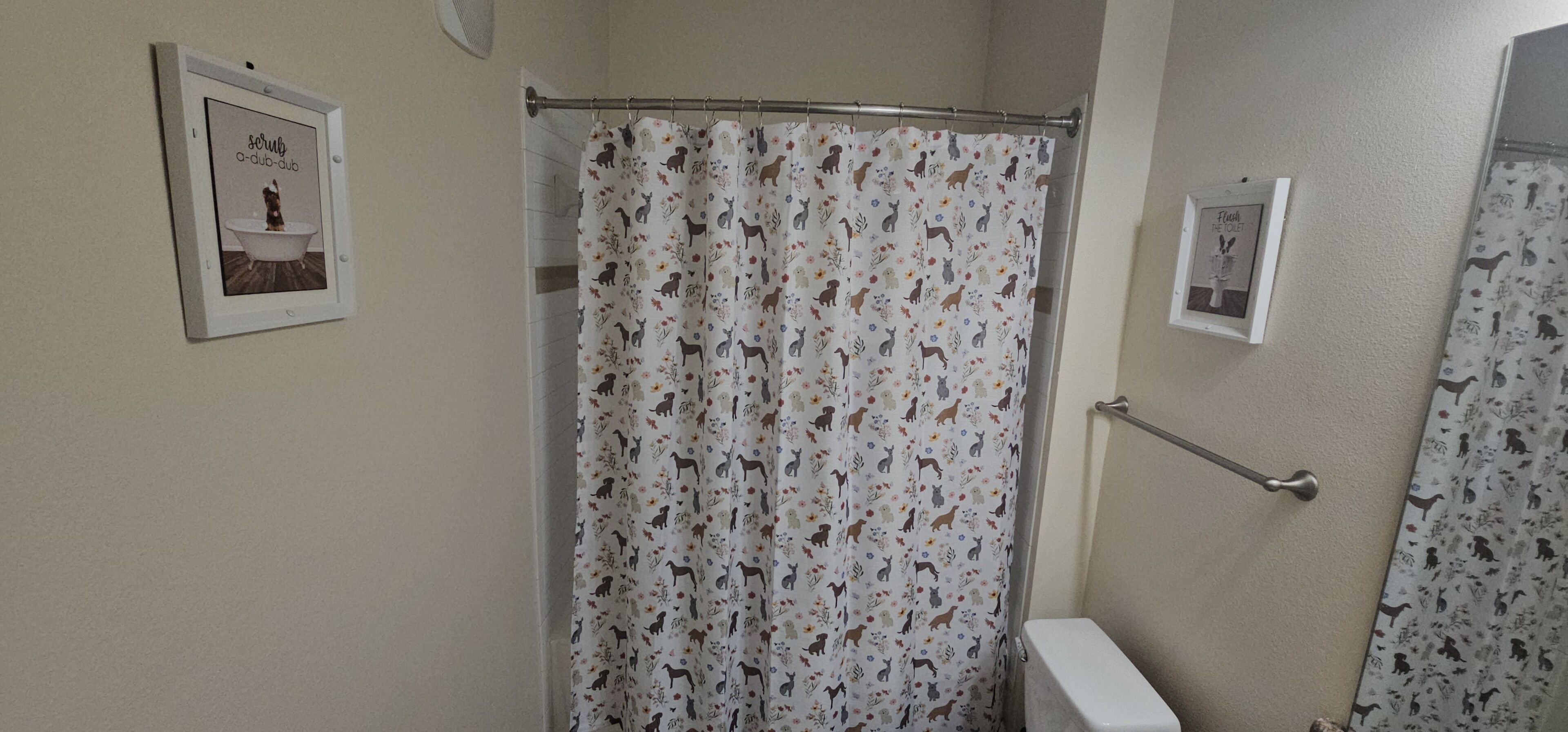 A bathroom with a shower curtain featuring animal prints, a framed picture on the wall, and a toilet.