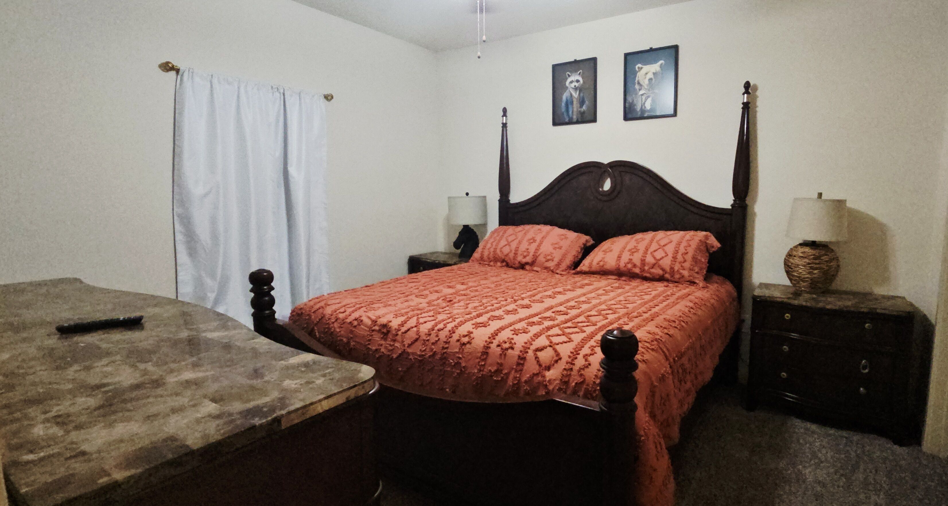 A bedroom with a bed, nightstands, a table, and a curtain.